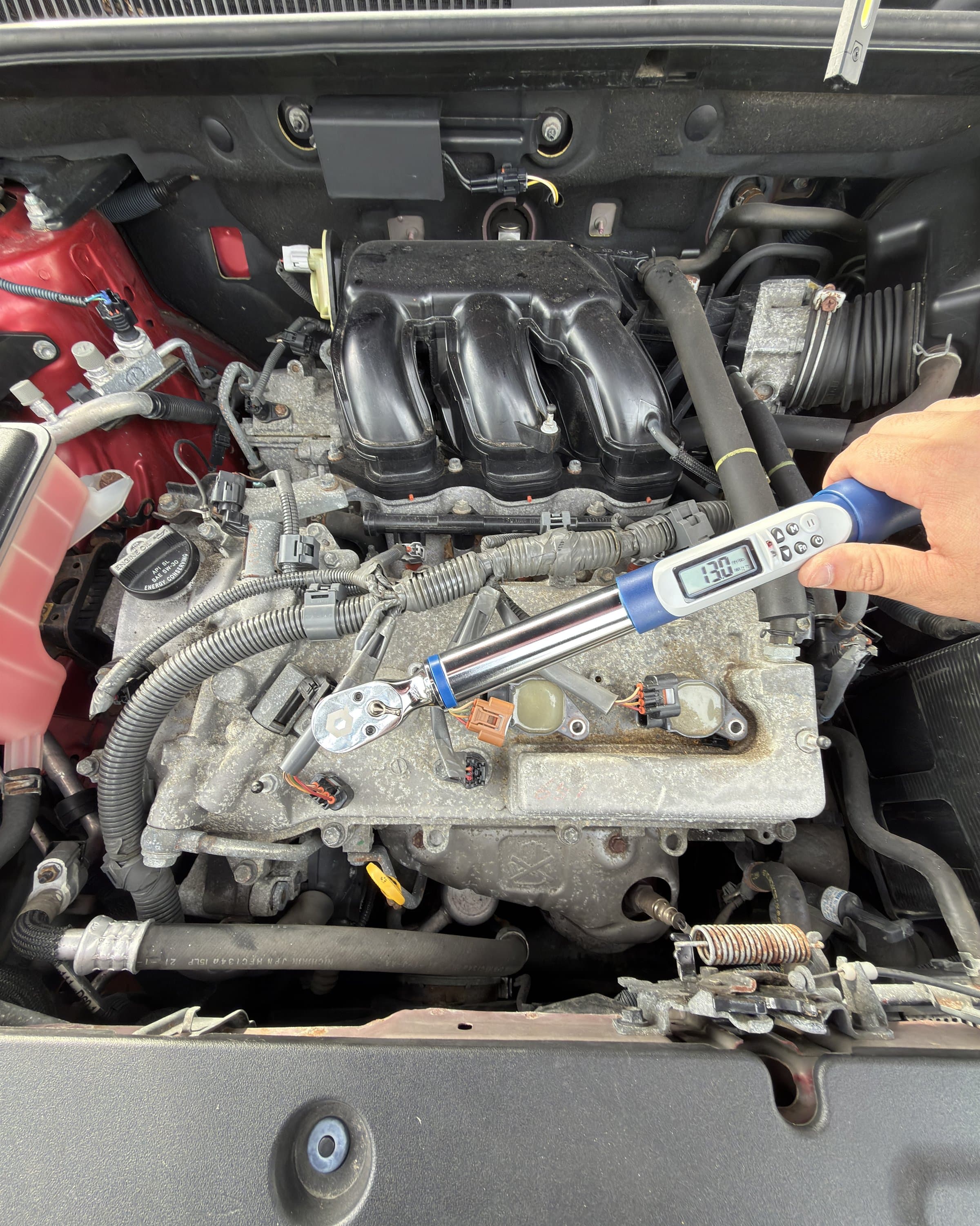 A hand using a digital torque wrench while working in an engine bay.