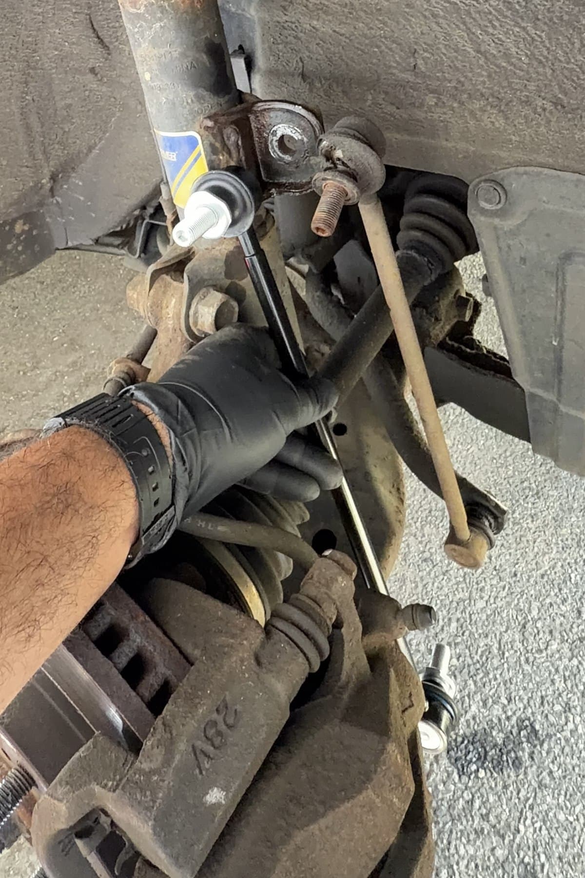 A gloved hand installing a suspension component inside a vehicle wheel well.